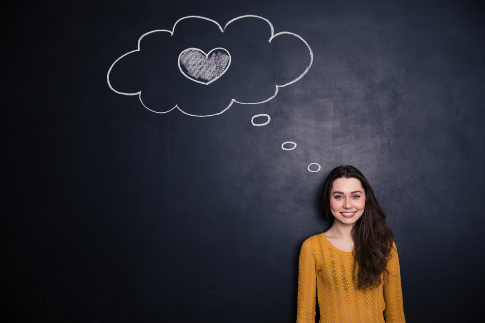 Beautiful happy young woman thinking about love and standing with blackboard behind her