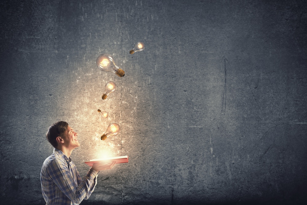 Young man holding opened book with glass glowing light bulbs flying out-1